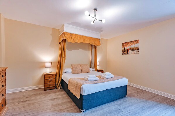 Une chambre à coucher avec un lit à baldaquin, des tables de chevet en bois, une commode et un tableau accroché au mur.