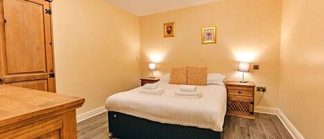 A bedroom with a bed, bedside tables, a wooden dresser, and a chandelier.