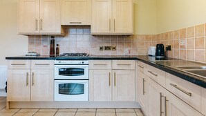 Une cuisine avec des meubles de couleur bois clair, un four double, une cuisinière à gaz et un dosseret carrelé.