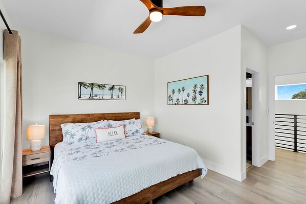 A bedroom with a wooden bed, two wall-mounted lamps, a ceiling fan, and two beach-themed wall art pieces.