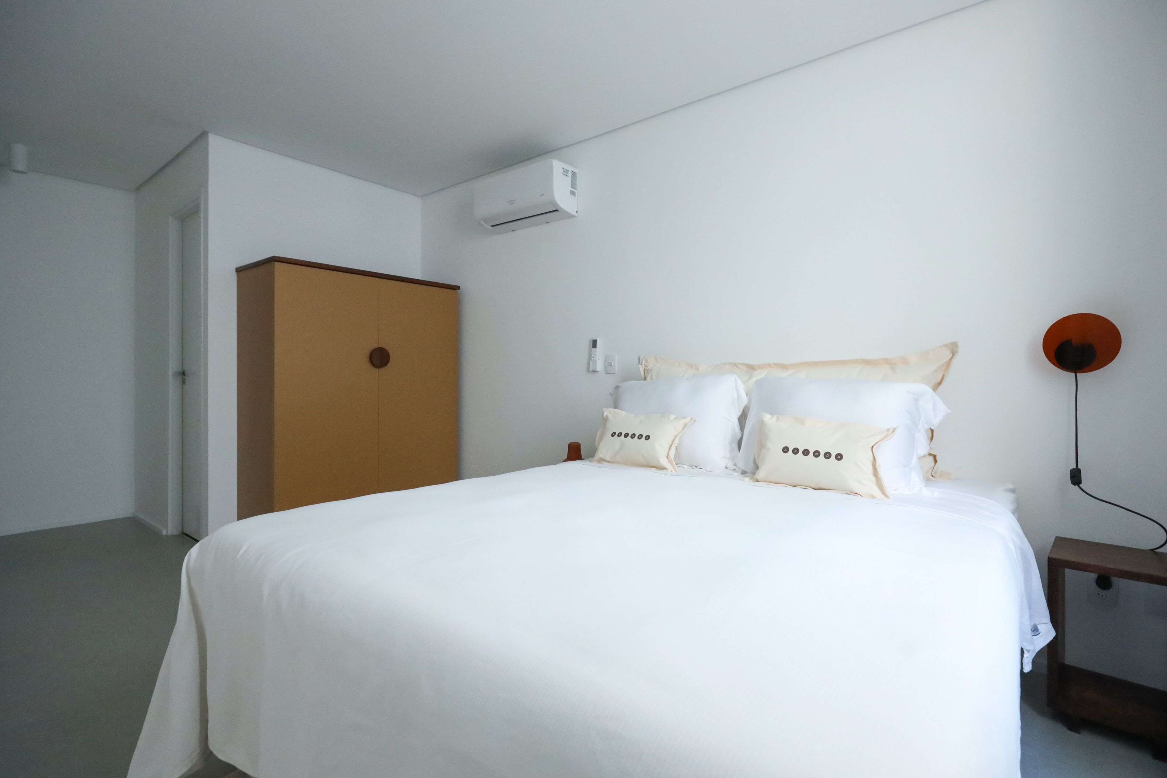 A bedroom with a bed, a wardrobe, an air conditioning unit, and a bedside table with a lamp.