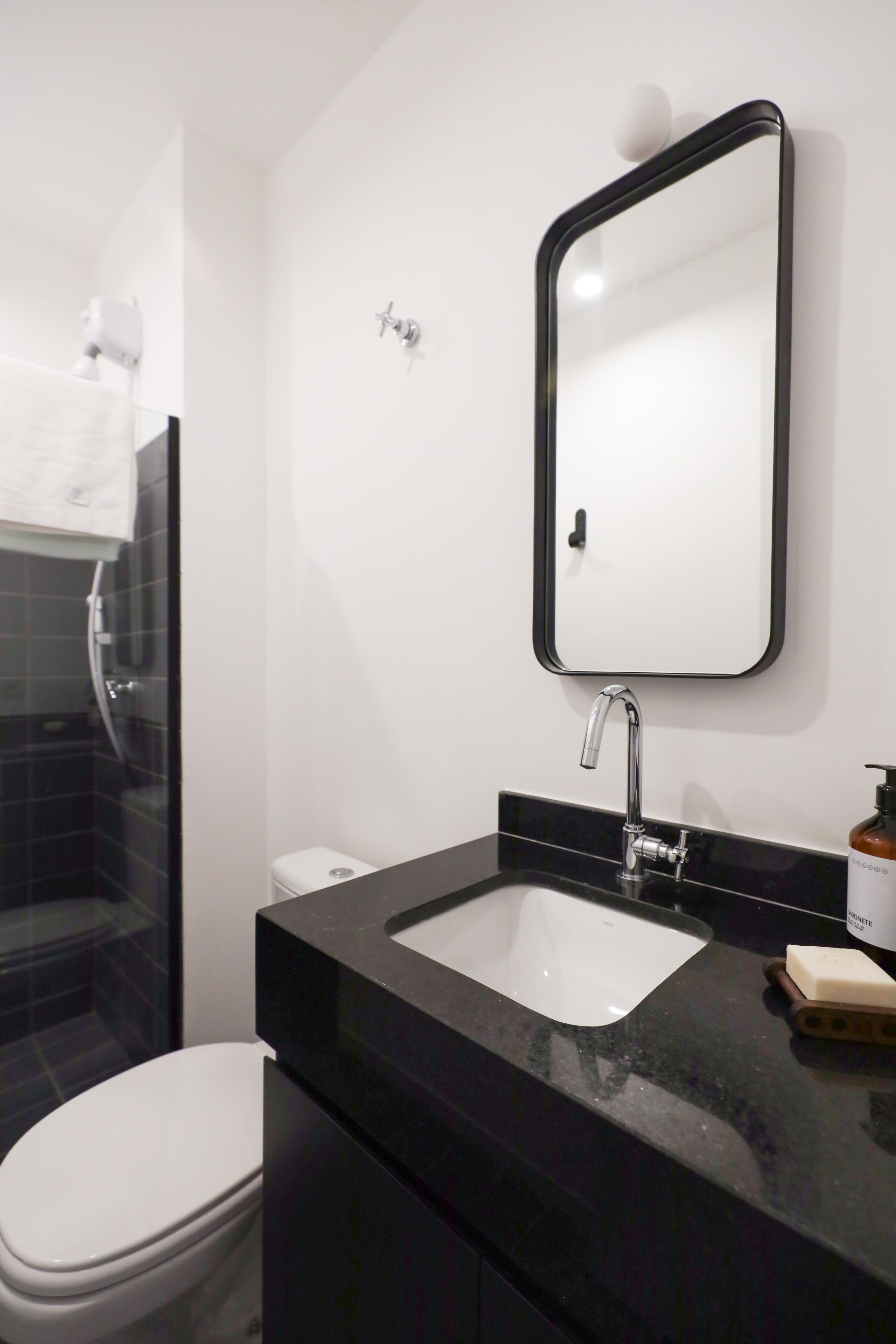 A modern bathroom with a black countertop, a white sink, a mirror, and a toilet.