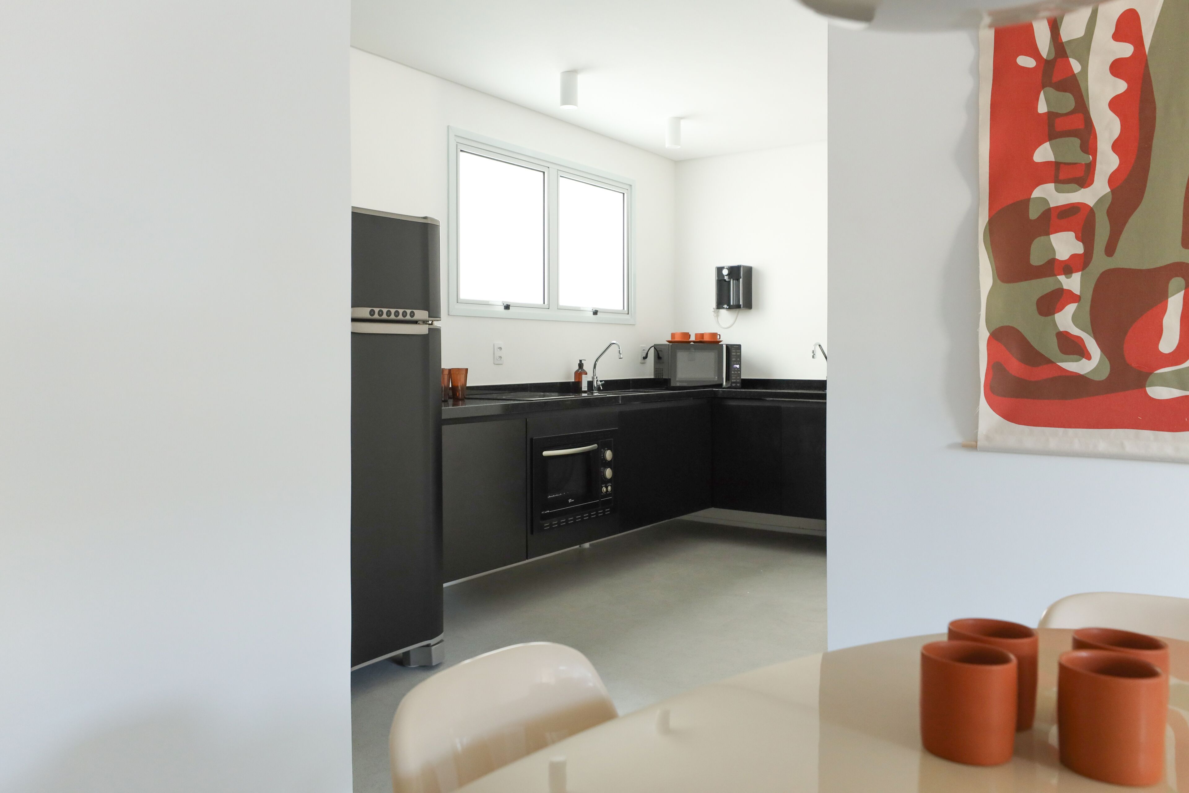 A modern kitchen with a refrigerator, oven, microwave, and sink. There is a window above the sink and a large abstract painting on the wall.