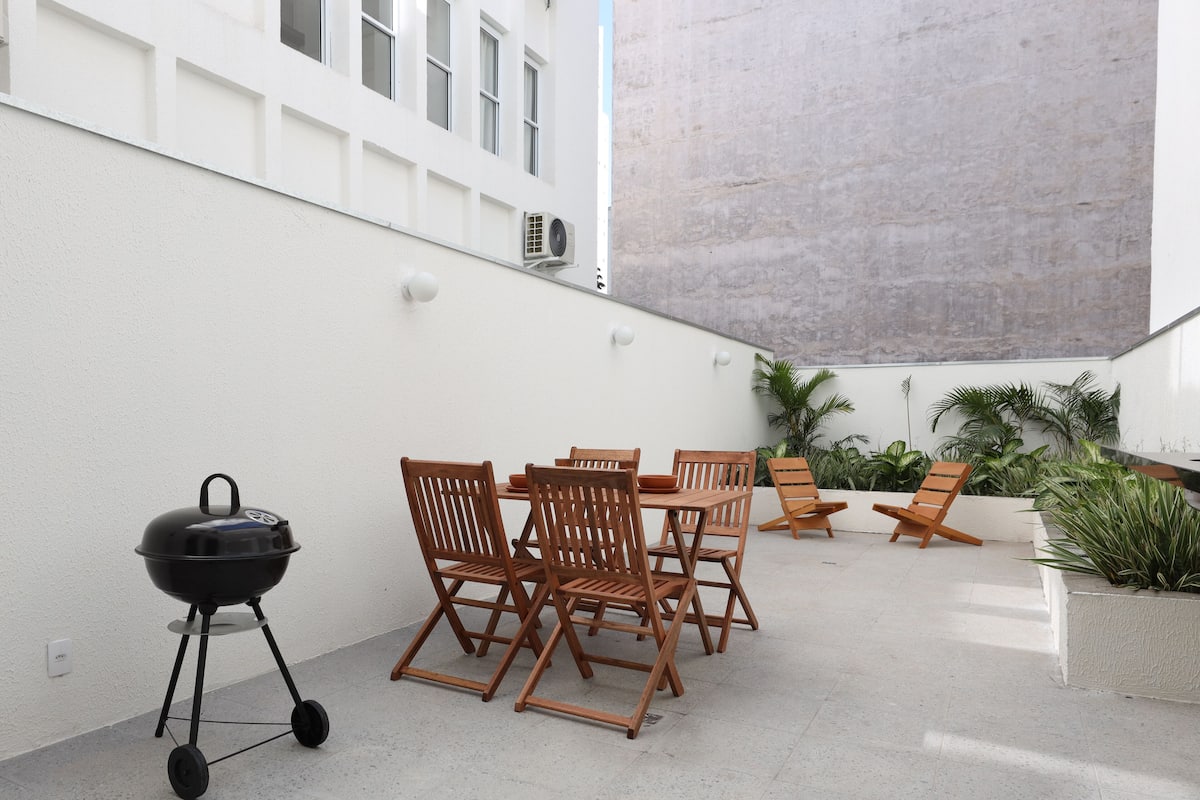 Eine Terrasse im Freien mit Grill, Holzstühlen und einem Tisch.