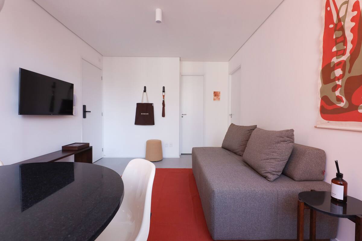 Ein modernes Wohnzimmer mit Flachbildfernseher, einer Couch, einem roten Teppich und einem kleinen Tisch mit einer Flasche.