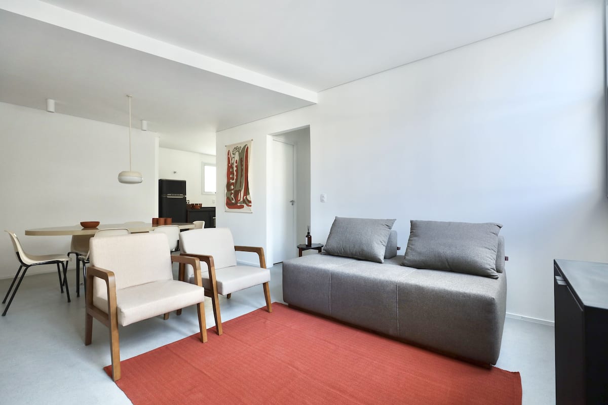 Ein zeitgemäßer Wohnbereich mit einer Couch, Sesseln, einem Esstisch und einer Küchenzeile.