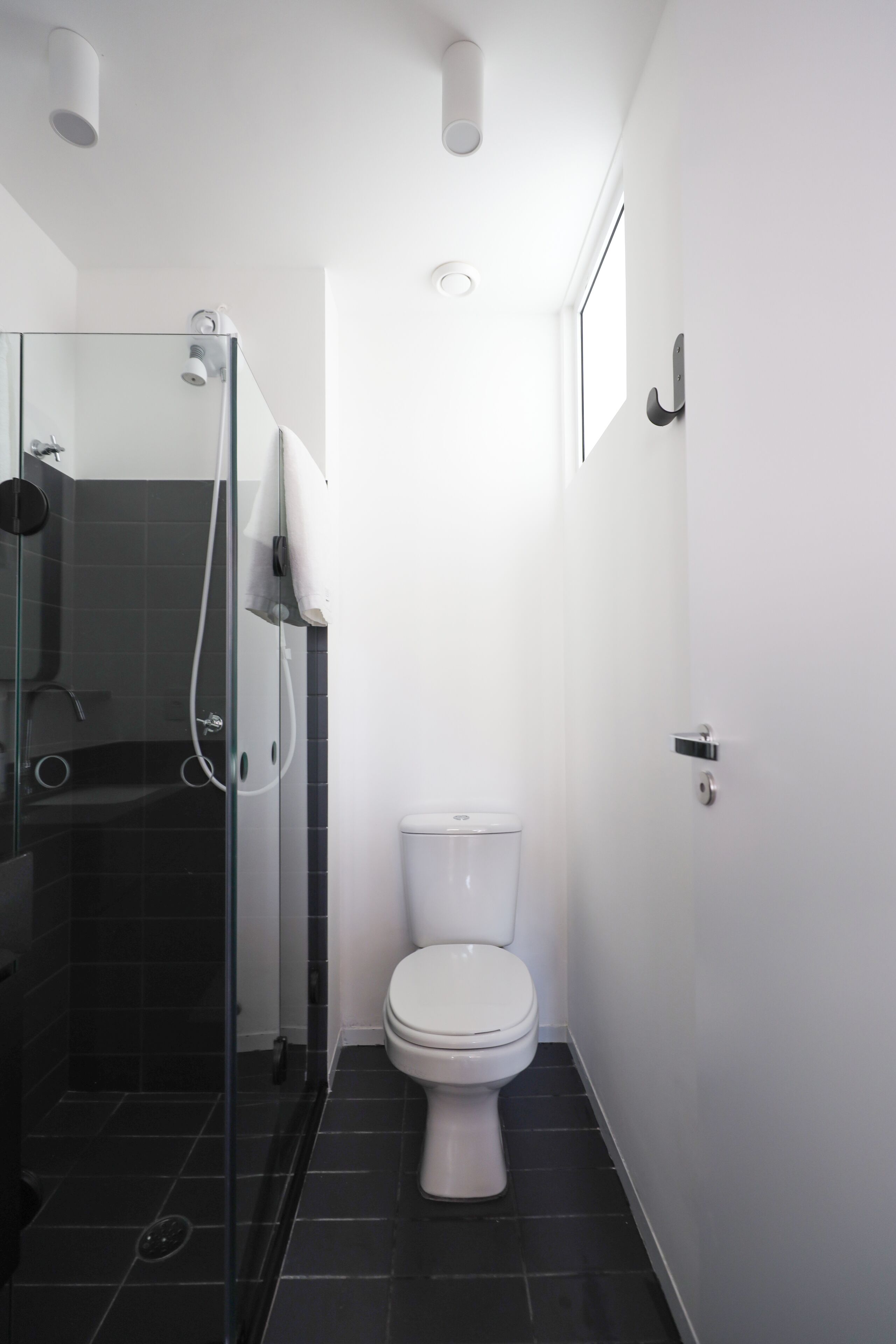 A modern bathroom with a glass-enclosed shower, a white toilet, and a dark tiled floor.