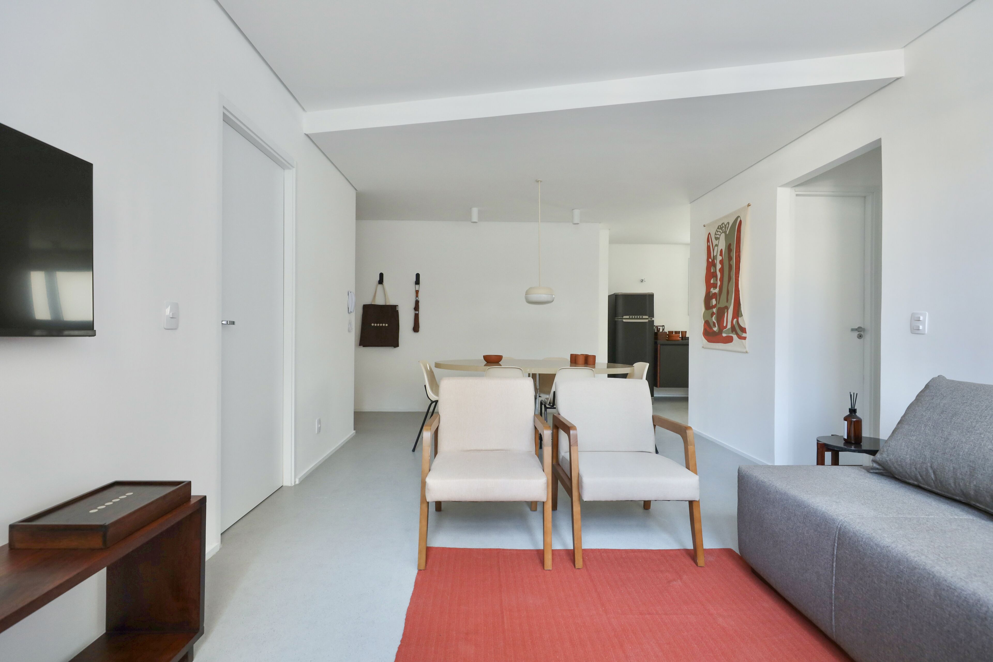 Ein modernes Wohnzimmer mit einem grauen Sofa, einem roten Teppich und einem Essbereich mit weißen Stühlen und einem Tisch.