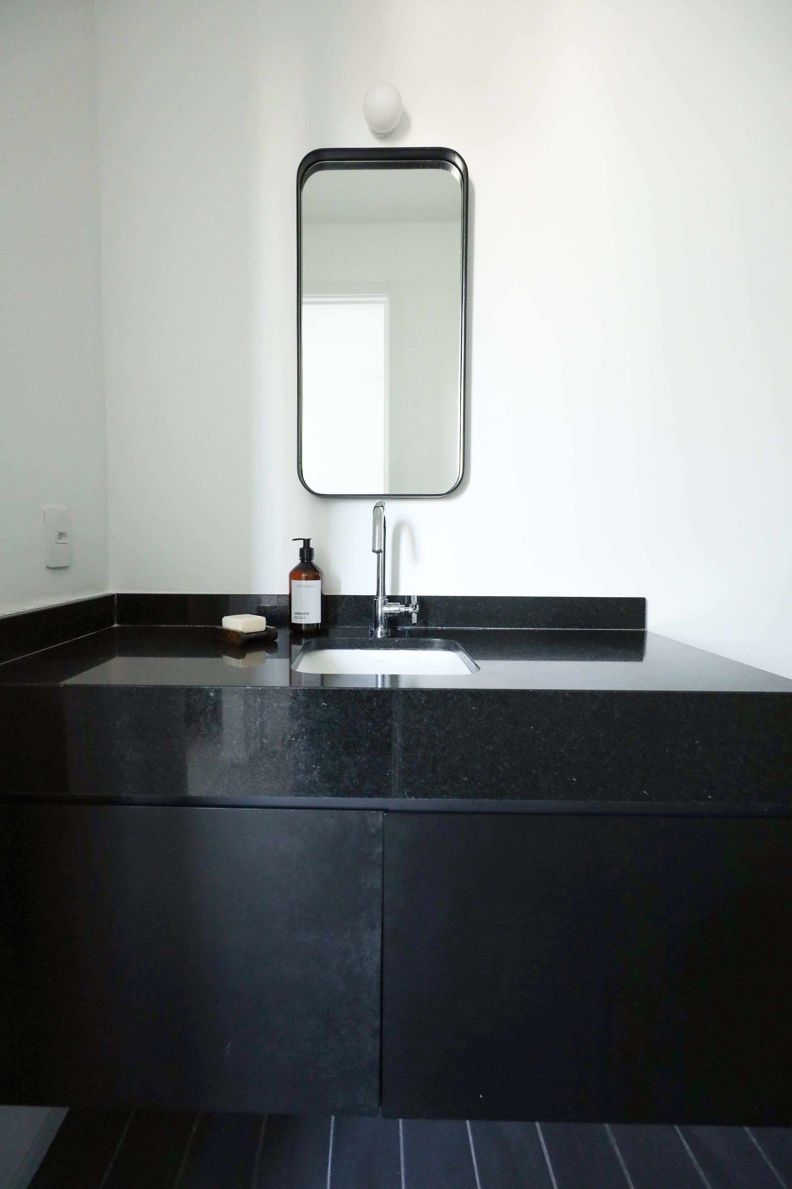 A modern bathroom with a black countertop, a sink, a mirror, and a soap dispenser.