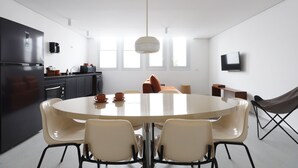 A modern kitchen with a central island, a dining area with a round table and chairs, and a flat-screen TV mounted on the wall.