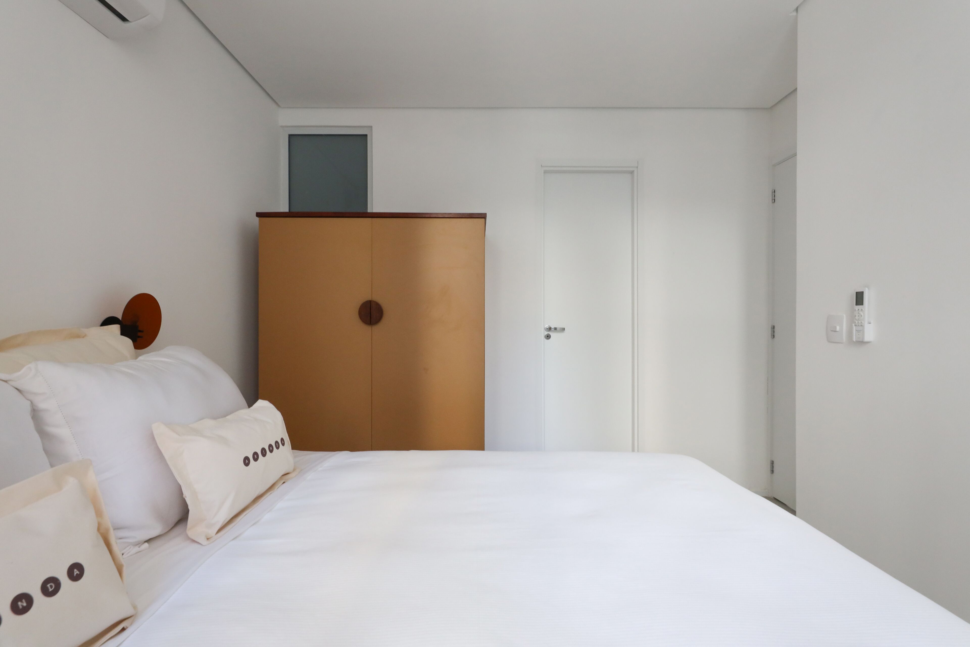 Een slaapkamer met een bed, witte kussens, een houten garderobe en een witte deur.