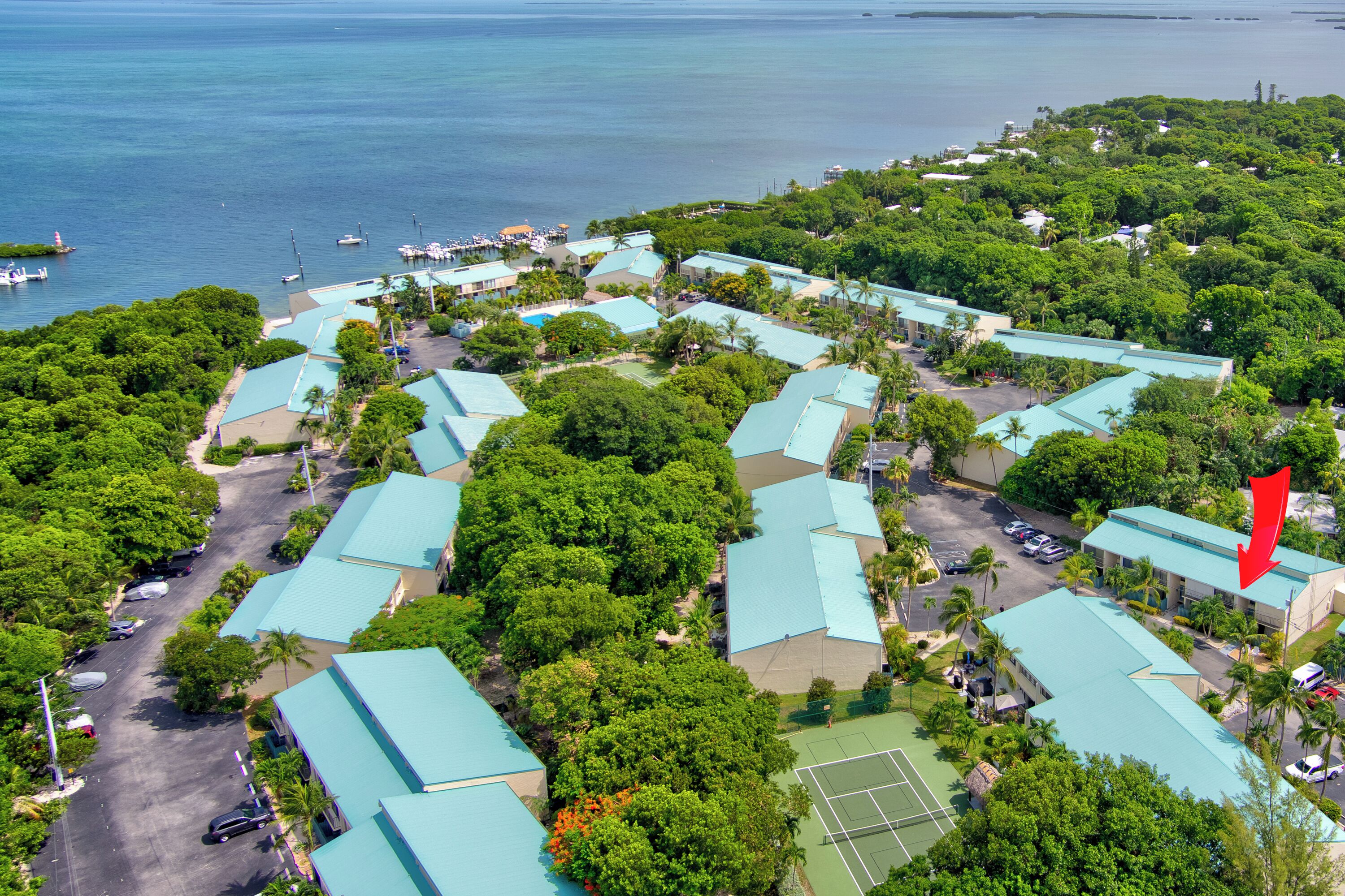 An aerial view of a resort with multiple buildings, a tennis court, and a marina.