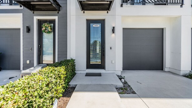 Una moderna casa a schiera con facciata grigia, due porte garage e un piccolo giardino antistante.