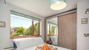Un dormitorio con una cama grande, una mesita de noche, un espejo y una ventana con vistas a zonas verdes.