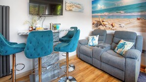 Una sala de estar con un sofá gris, dos taburetes azules, un televisor de pantalla plana y un mural con temática de playa.