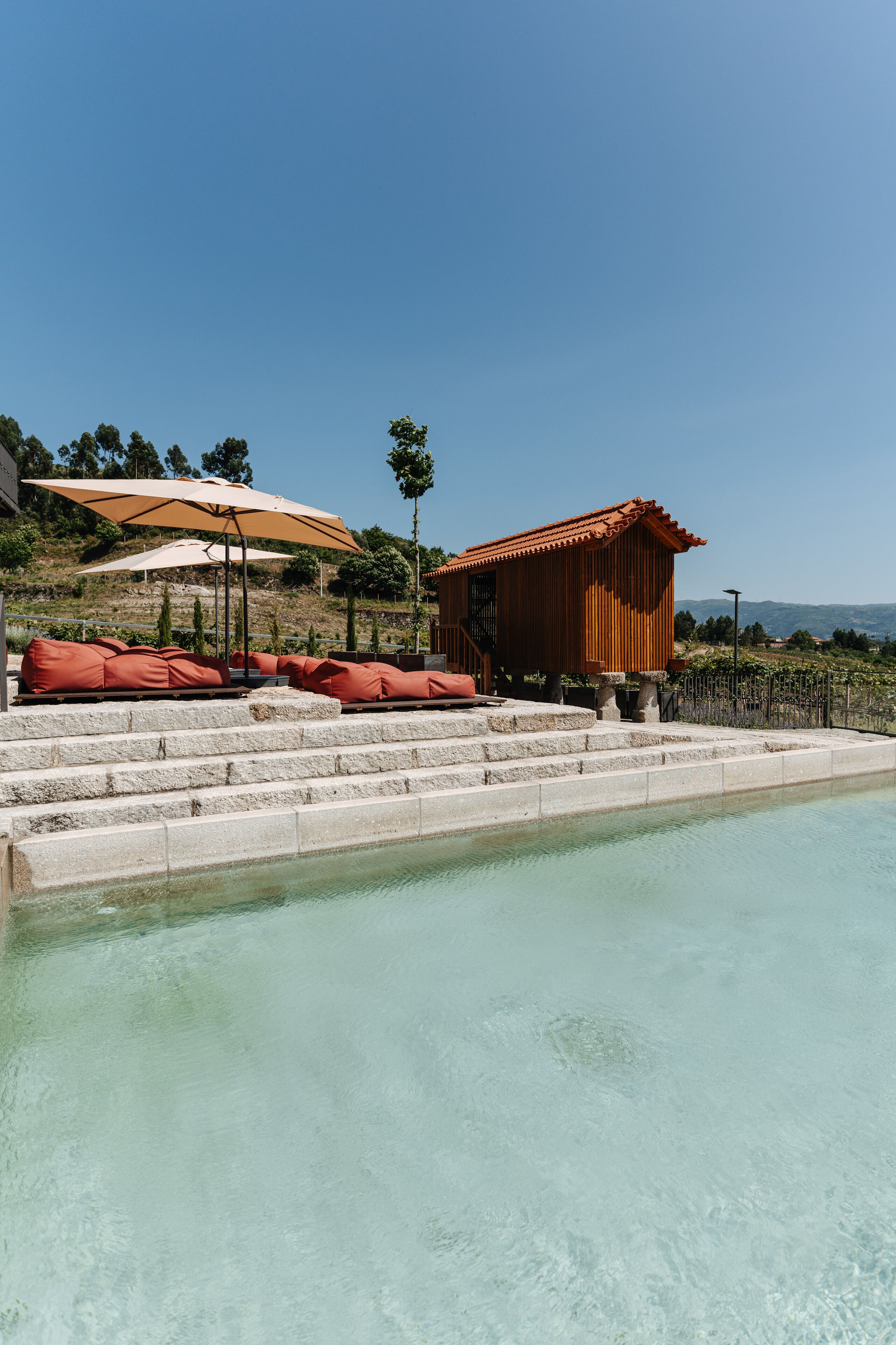 Un espace piscine avec des marches descendant vers l’eau, entouré de chaises longues rouges et de parasols.
