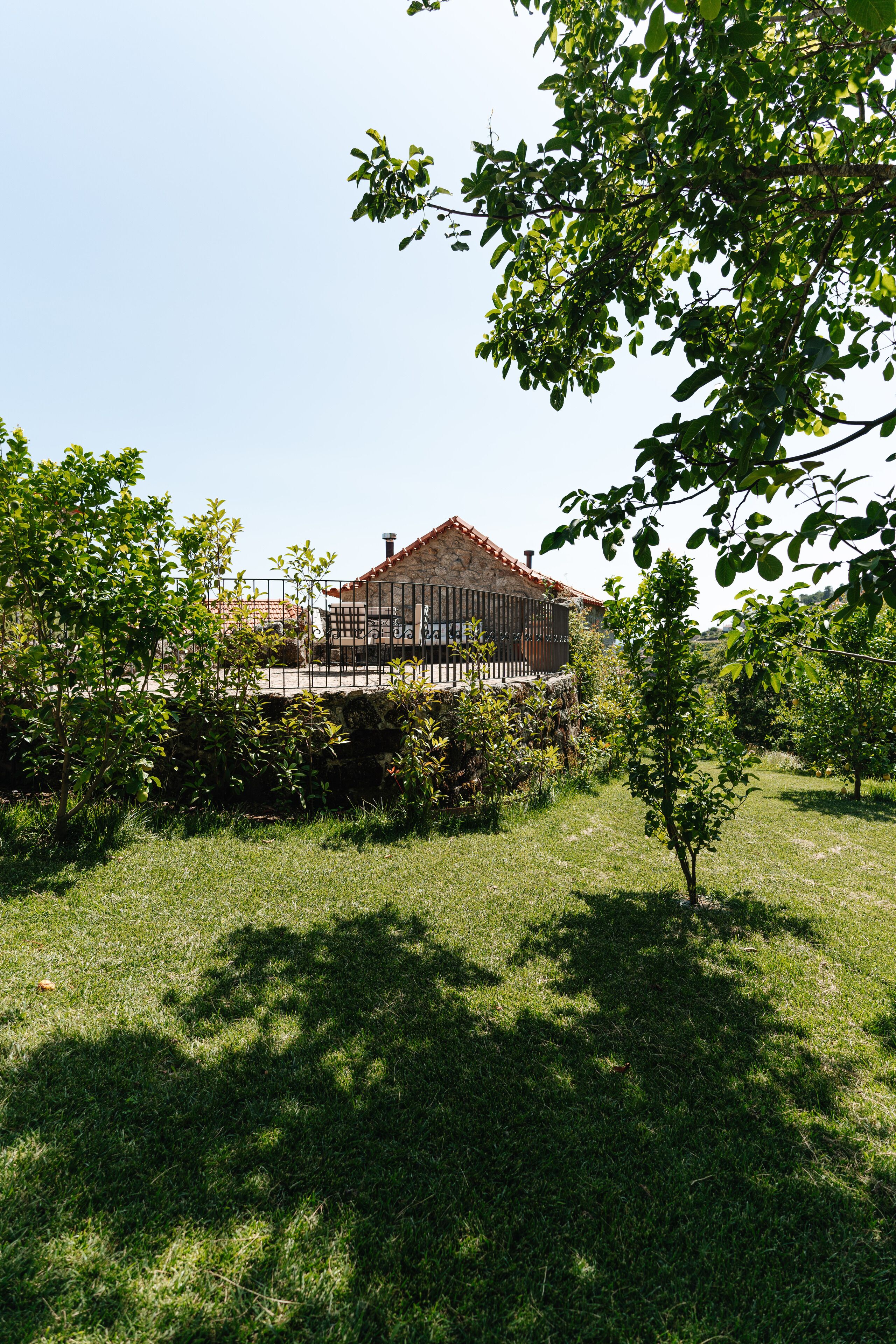 A stone house with a tiled roof, surrounded by a stone wall and a metal fence.