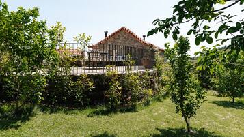 A stone house with a tiled roof, surrounded by a stone wall and a metal fence.
