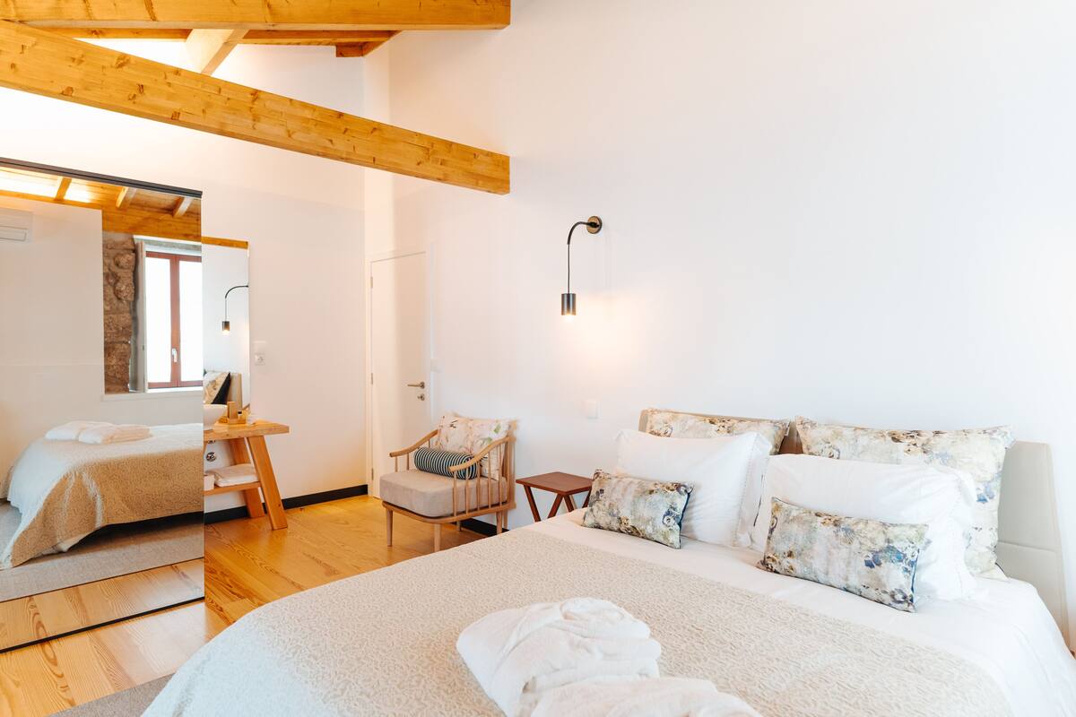 Ein Schlafzimmer mit einem großen Bett, einem Holzstuhl, einem kleinen Tisch und einer Wandlampe.