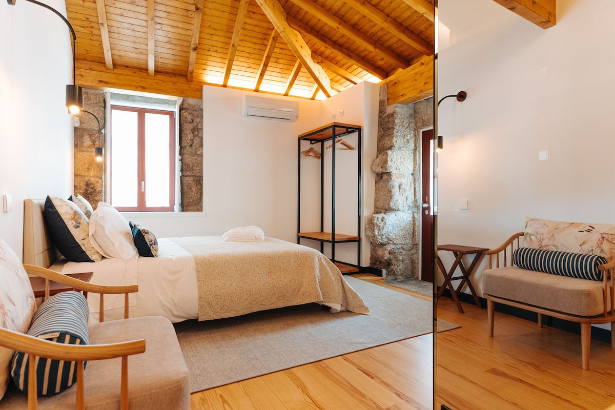 Ein Schlafzimmer mit einem Bett, einem Holzstuhl, einer Couch, einer Steinwand und einem Fenster.