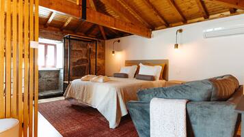 Een slaapkamer met een bed, een grijze bank, een houten plafond en een stenen muur.