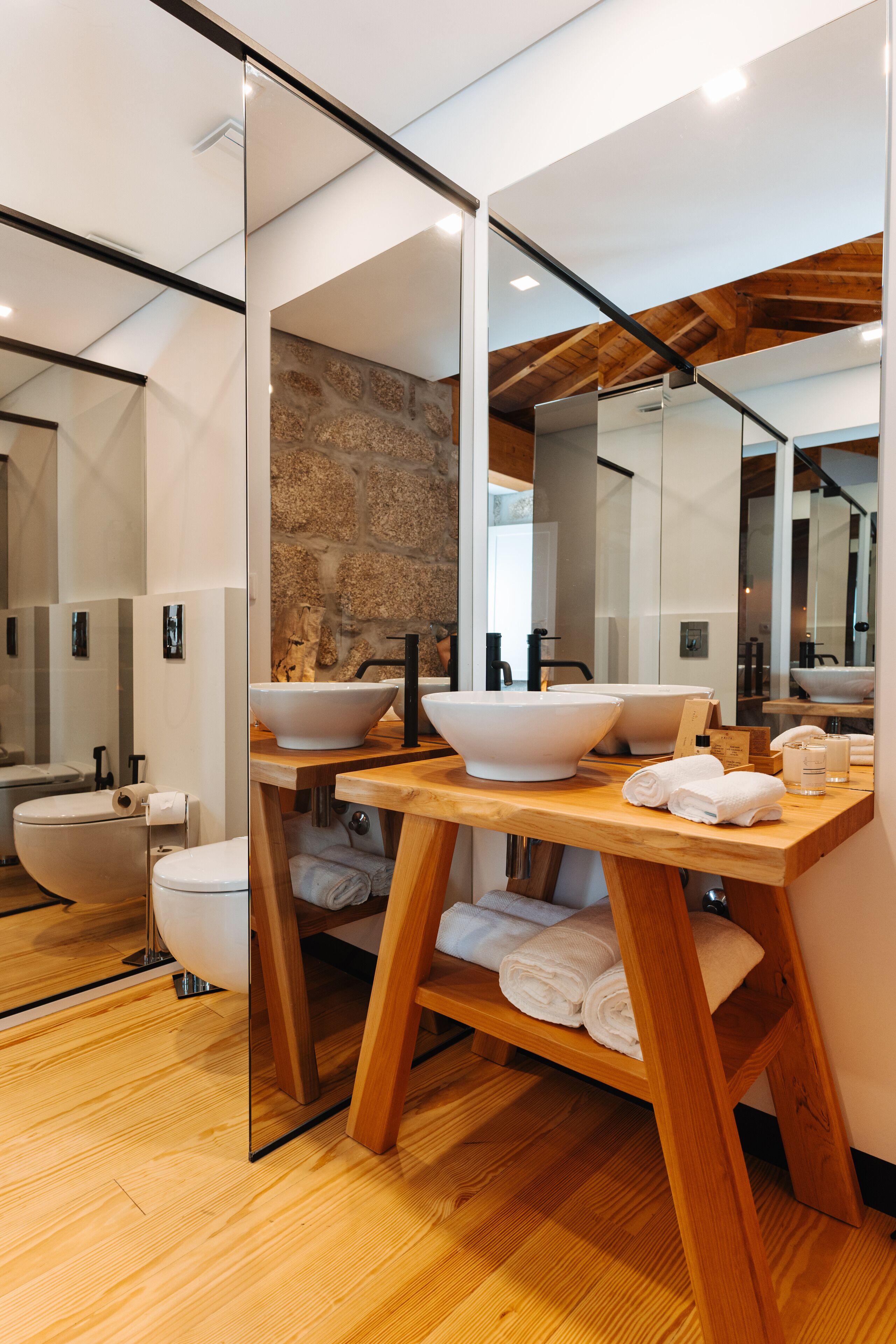 A modern bathroom with a wooden vanity, large white sinks, and a stone accent wall.
