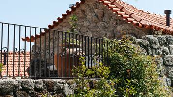 A stone building with a tiled roof, a metal fence, and lush greenery.