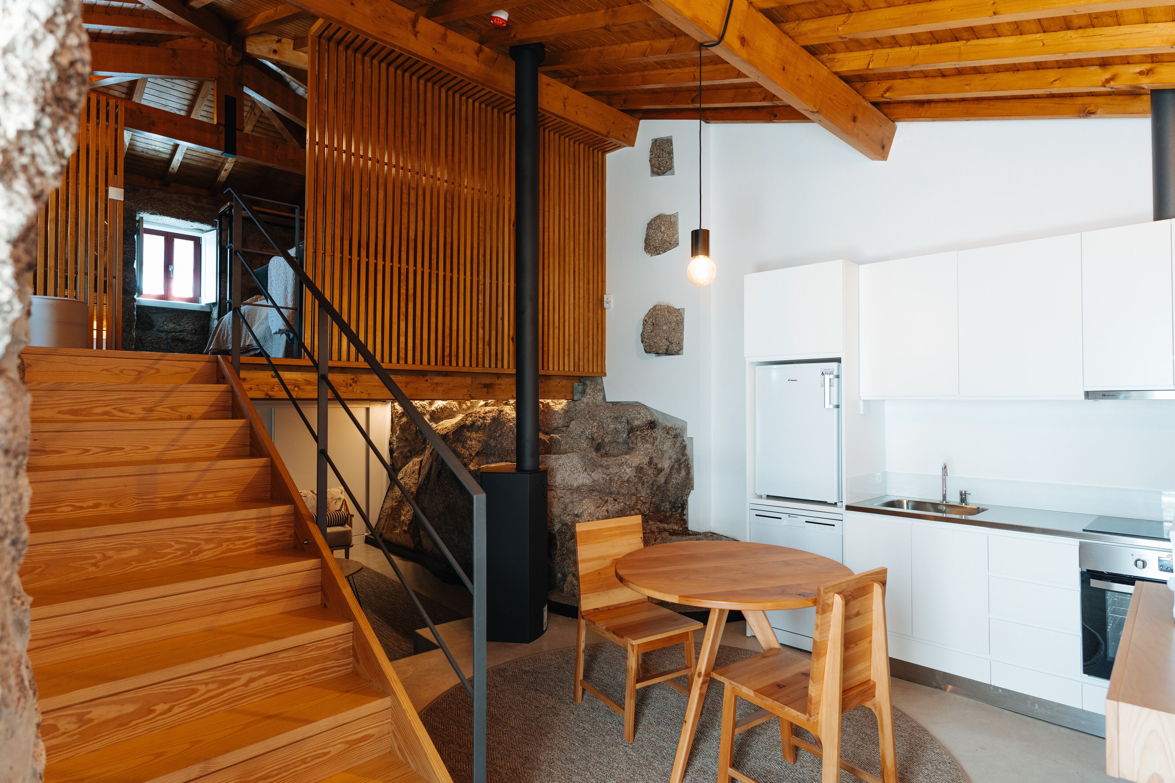 A wooden staircase leading to a kitchen area with white cabinets and a stone wall.