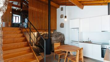 Una escalera de madera conduce a una zona de cocina con armarios blancos y una pared de piedra.