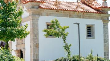 Un edificio histórico con tejado de tejas, muros de piedra y un jardín con diversas plantas.