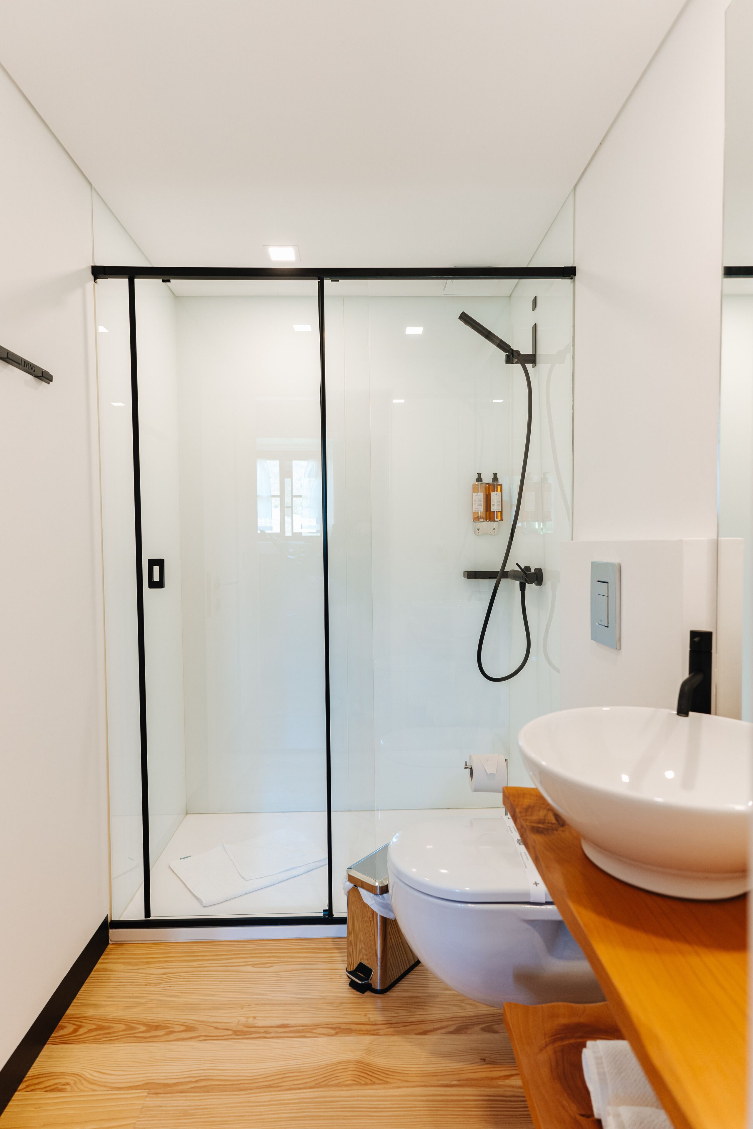A modern bathroom with a glass shower enclosure, a white toilet, and a wooden vanity with a white sink.