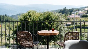 A balcony with wicker chairs and a small round table, overlooking a scenic landscape with hills and houses. - D'Autor Village (Baiao)
