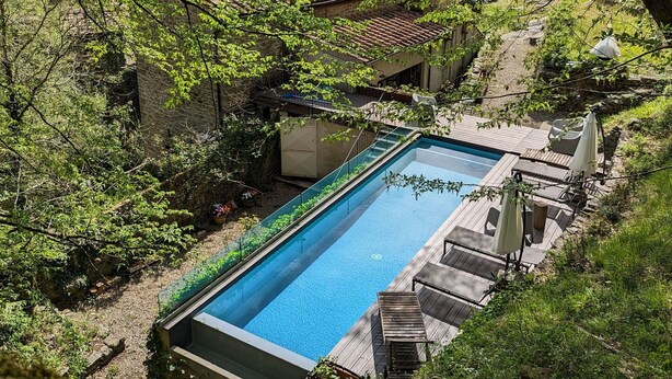 A swimming pool surrounded by lush greenery and stone buildings.