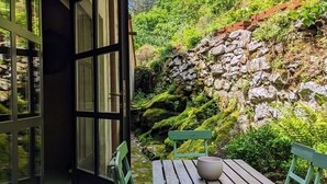 A patio with a table and chairs, a stone wall, and a view of a lush green hillside.