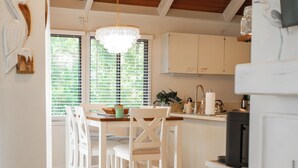 A modern kitchen with white cabinetry, a wooden ceiling, and a dining area with white chairs.