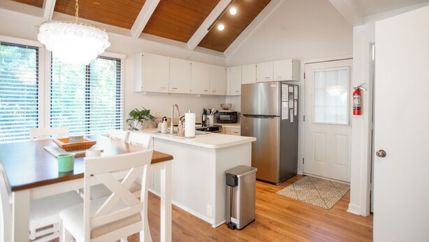 A modern kitchen with white cabinetry, a stainless steel refrigerator, and a wooden ceiling.