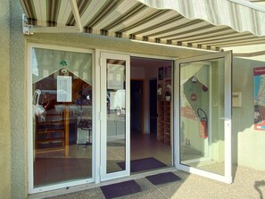 Une entrée d’immeuble avec des portes vitrées, un sol carrelé et un petit espace extérieur doté d’un paillasson.