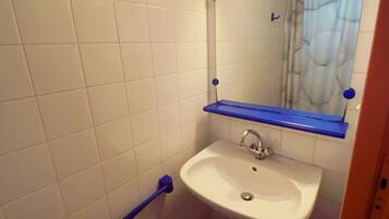 Een badkamer met witte betegelde wanden, een witte wastafel, een blauwe handdoekhouder, een blauwe handgreep en een witte prullenbak.