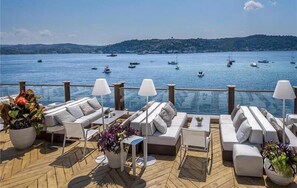 Um terraço com sofás e mesas brancas, com vista para uma marina com barcos.