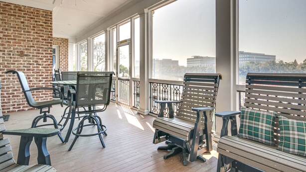 A covered outdoor area with a brick wall, a ceiling fan, and a view of a cityscape through large windows. - Riverfront North Augusta Home w/ Private Pool! (North Augusta)