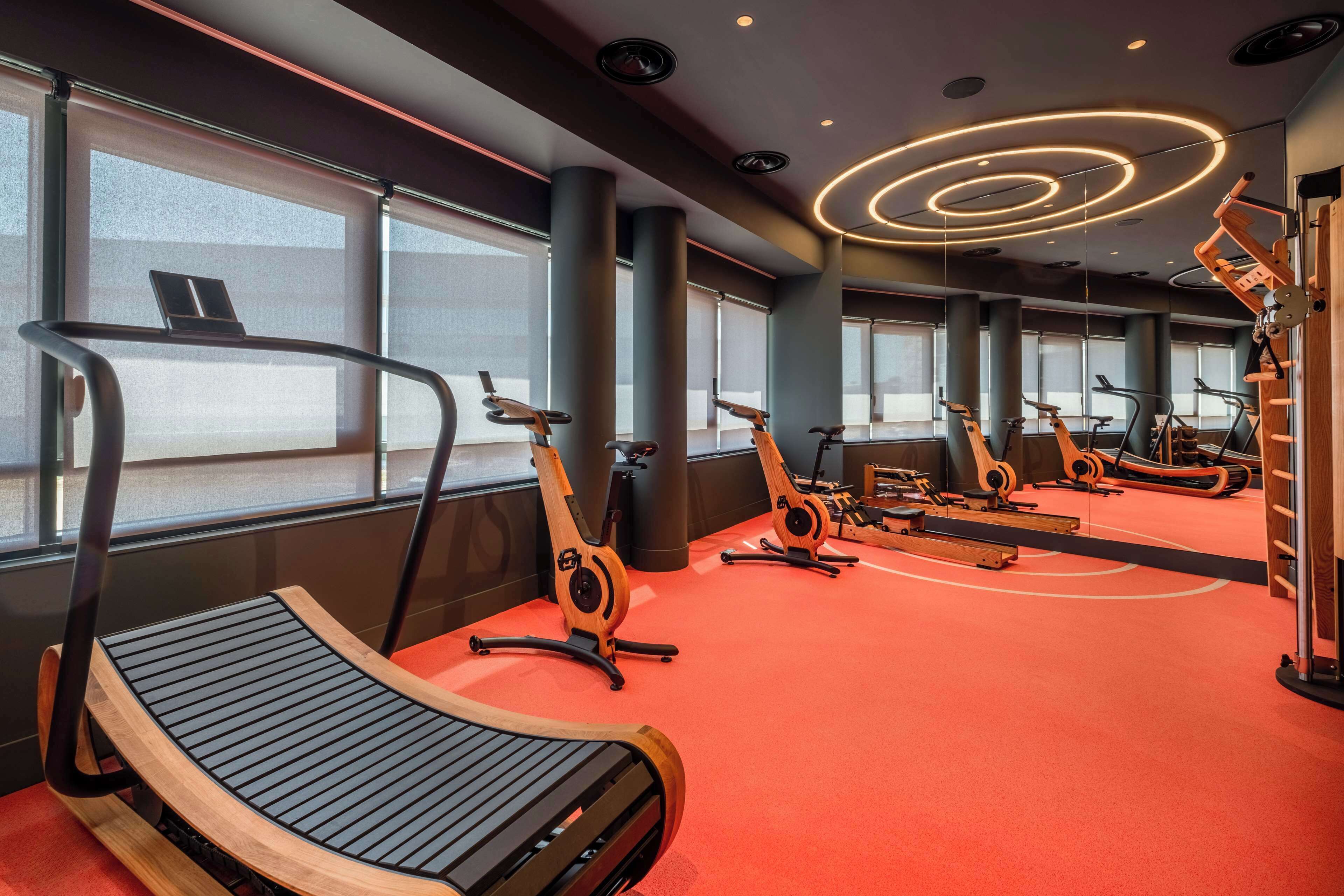 A gym with exercise equipment, large windows, and a red carpet.