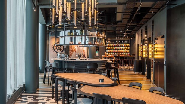 Un bar moderno con una barra alargada, diversas opciones de asientos y un suelo estampado.