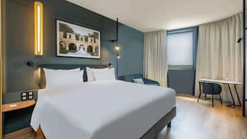 Ein modernes Hotelzimmer mit einem großen Bett, einem Schreibtisch und einem Sessel. An der Wand hängt ein Gemälde, und ein Fenster ist mit Vorhängen versehen.
