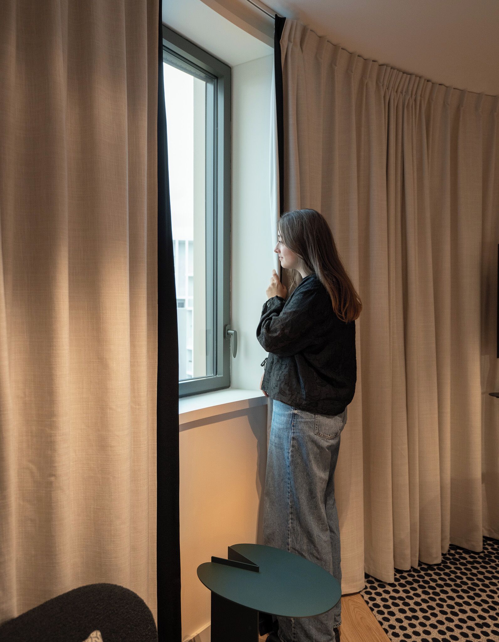 Una habitación con ventana, cortinas, una mesita y suelo estampado.