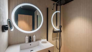 A modern bathroom with a white sink, two round mirrors with lights, a handheld showerhead, and a towel on the counter.