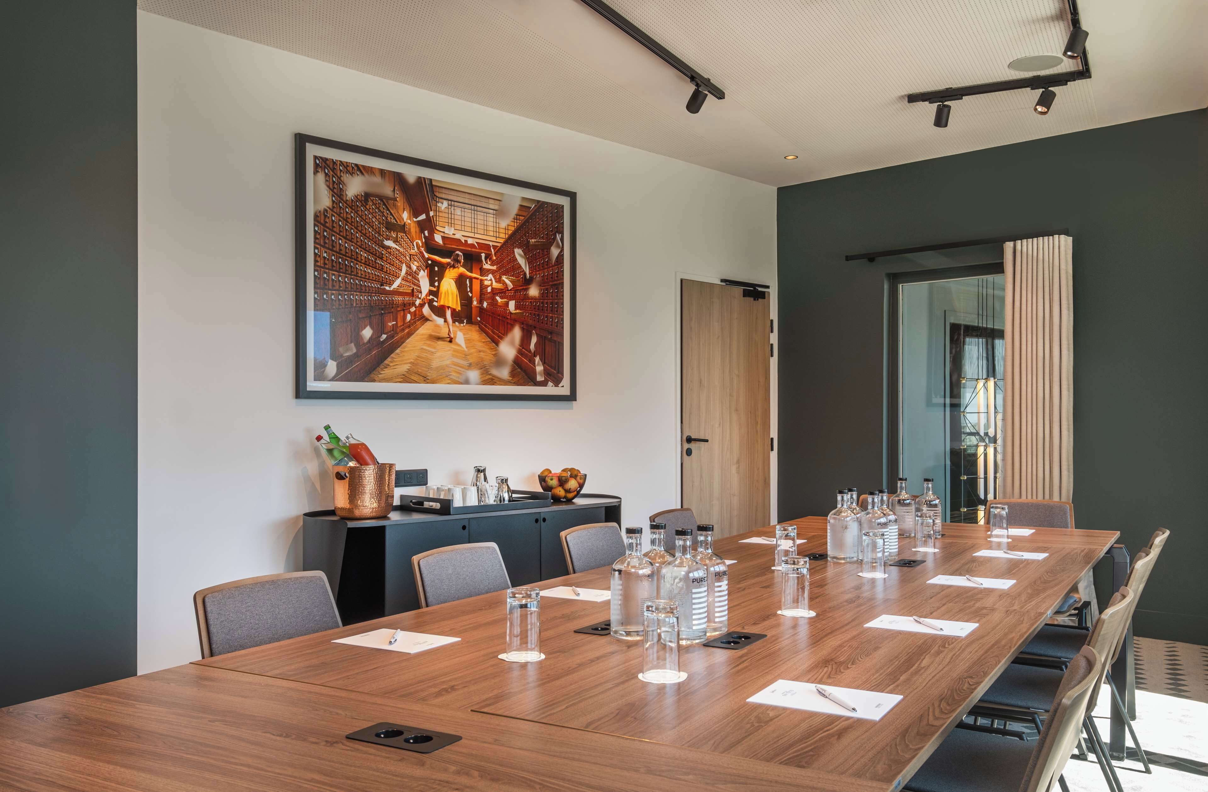 Une salle de conférence avec une longue table en bois, des chaises et un grand tableau encadré au mur.
