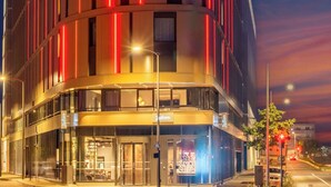 Un hotel moderno con fachada curva, varios pisos y líneas verticales rojas iluminadas.