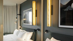 Une chambre d’hôtel avec deux lits, un grand tableau encadré au mur et un luminaire moderne.