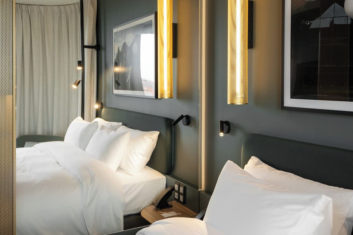 Une chambre d’hôtel avec deux lits, un grand tableau encadré au mur et un luminaire moderne.