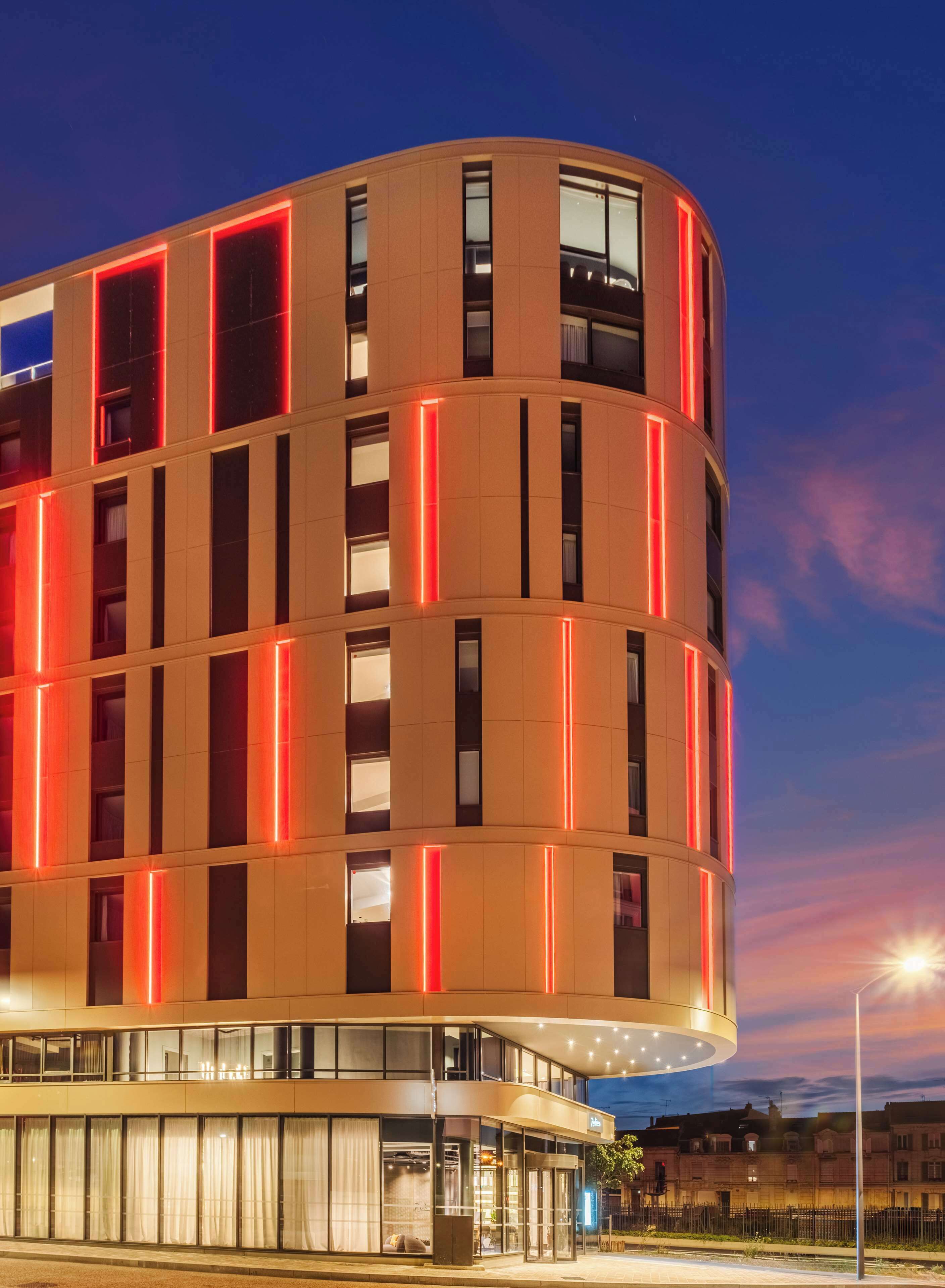 A modern hotel with a curved facade, multiple balconies, and a glass entrance.
